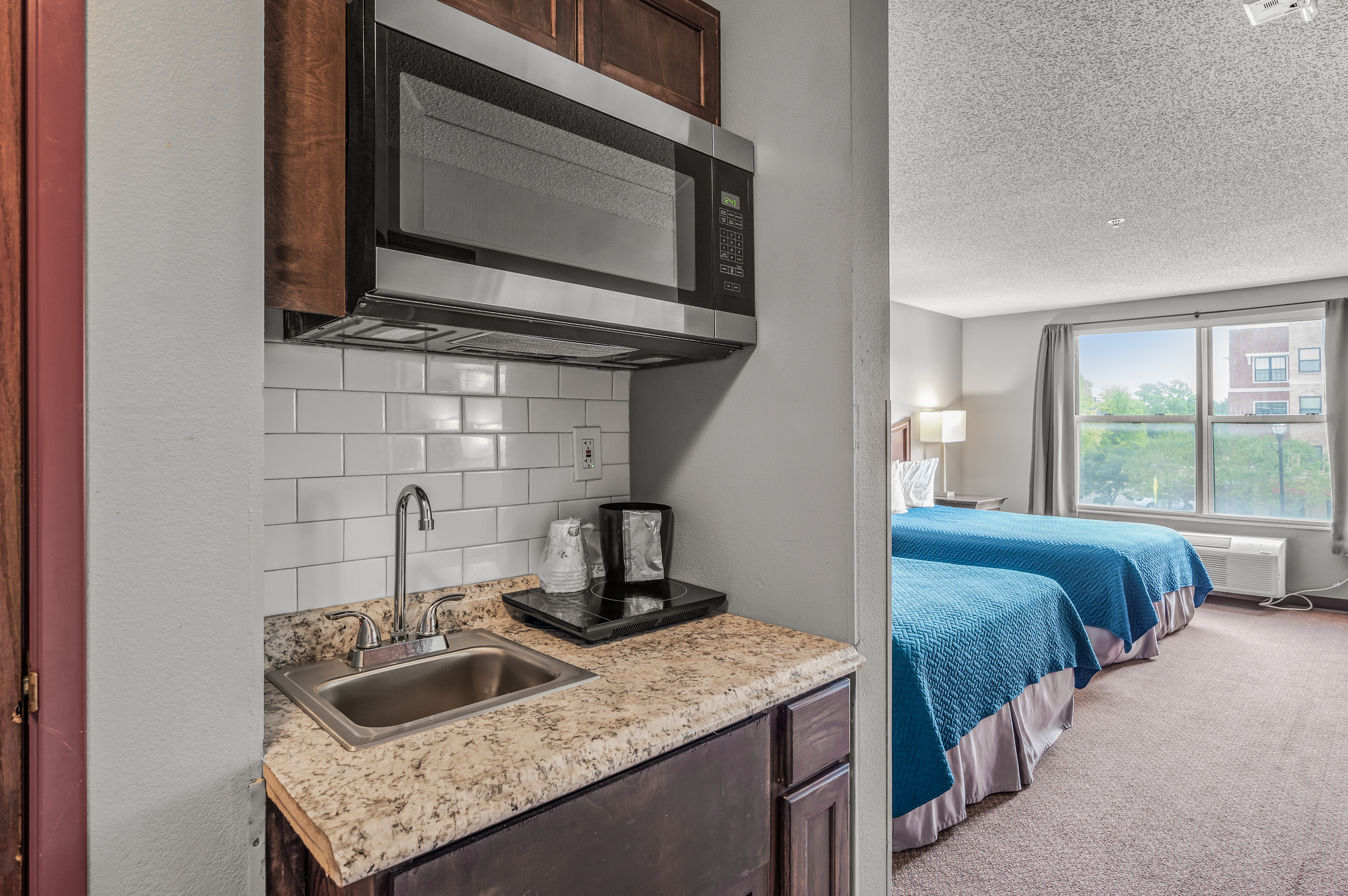 Kitchenette opening into a bright suite bedroom with two beds at TownSquare Place